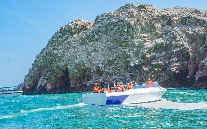 Bote turístico navegando frente a las formaciones rocosas de las Islas Ballestas en Paracas