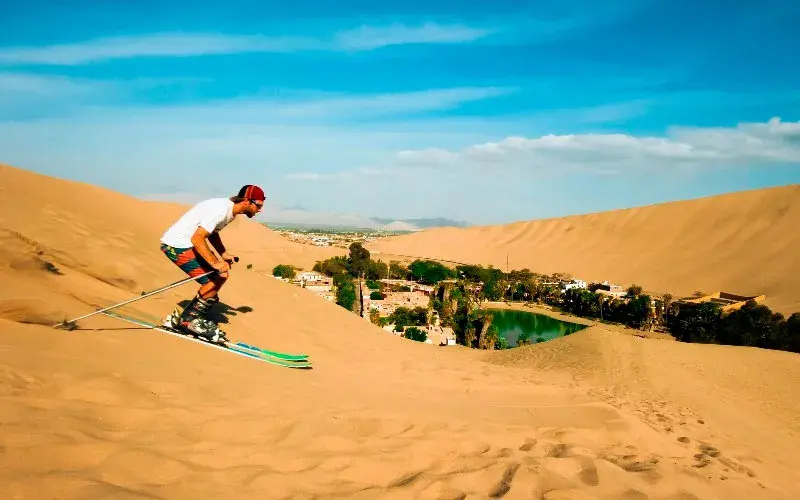 Persona practicando sand ski en las dunas con vista a la Laguna Huacachina en Ica