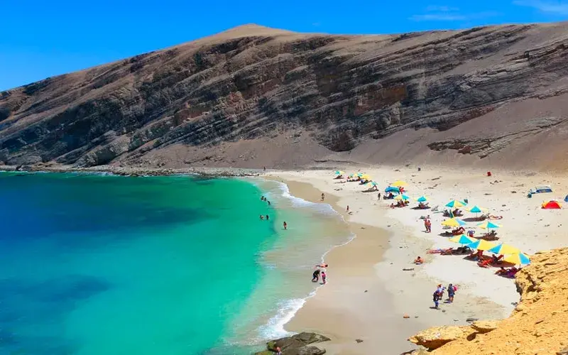 Vista panorámica de Playa La Mina en la Reserva Nacional de Paracas con mar turquesa y visitantes en la orilla