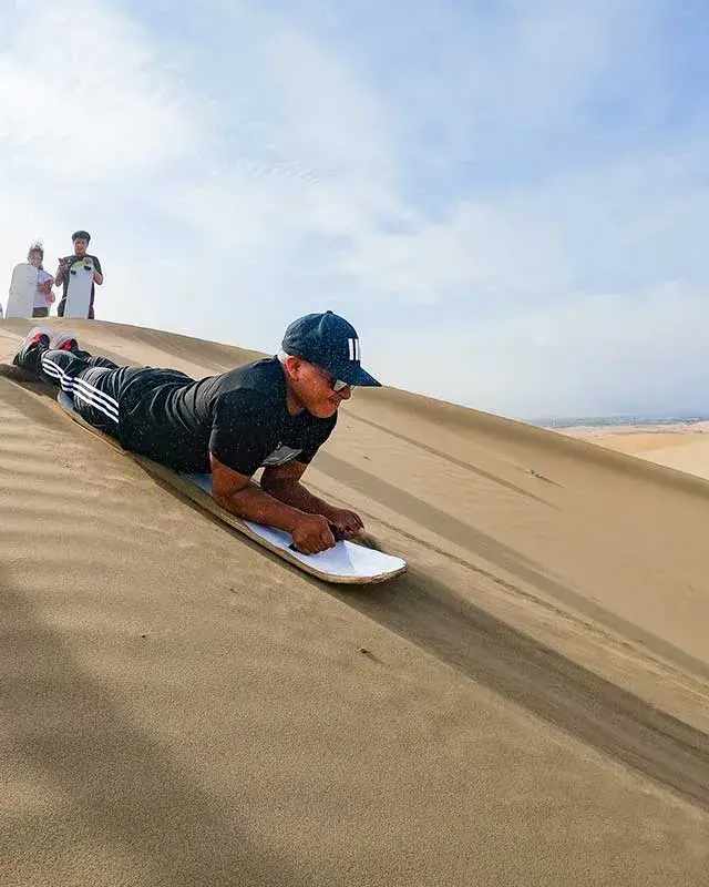 Turista practicando sandboarding en posición boca abajo en las dunas de Huacachina durante el Full Day Yakupark y Huacachina desde Lima