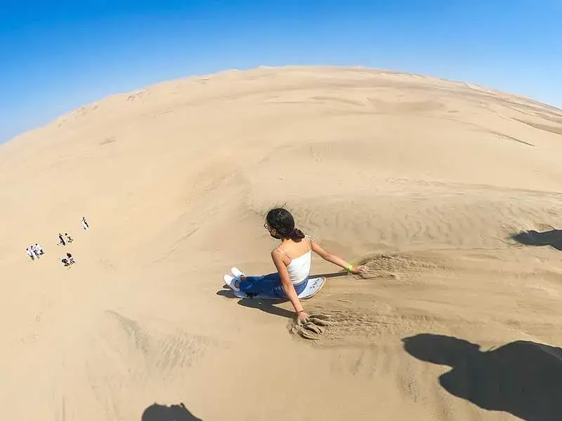 Turista practicando sandboarding en las dunas de Huacachina durante el Full Day Paracas Ica Chincha desde Lima