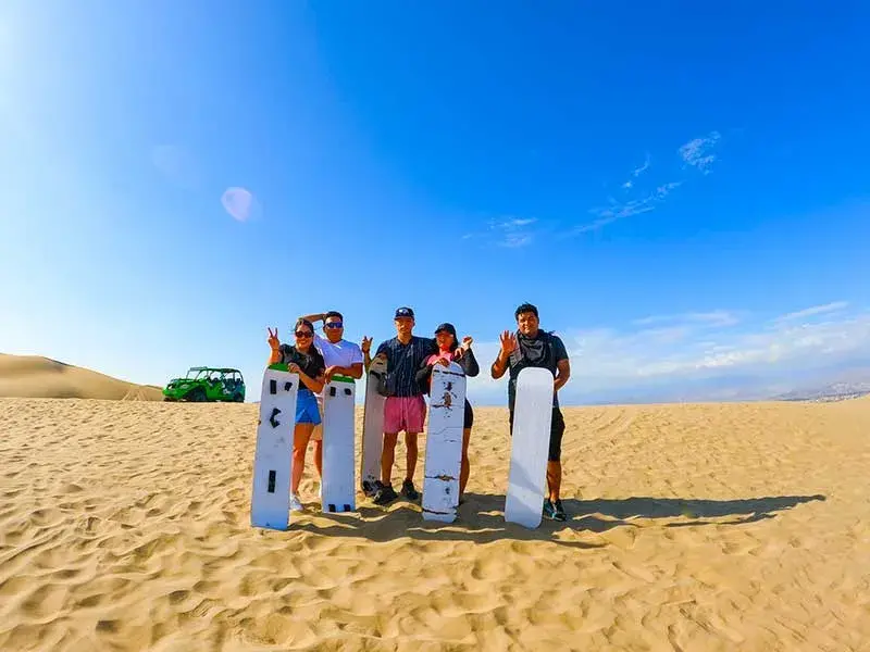 Grupo de turistas con tablas de sandboarding en las dunas de Huacachina durante el Tour 2 dias Paracas Ica con Hotel en Paracas desde Lima