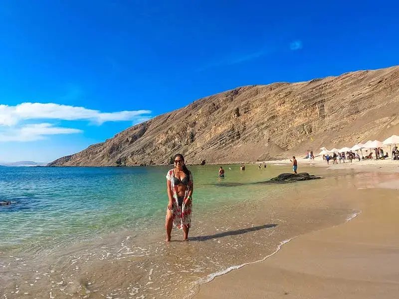 Turista posando en la orilla de Playa La Mina en Paracas con aguas cristalinas y cerros desérticos al fondo