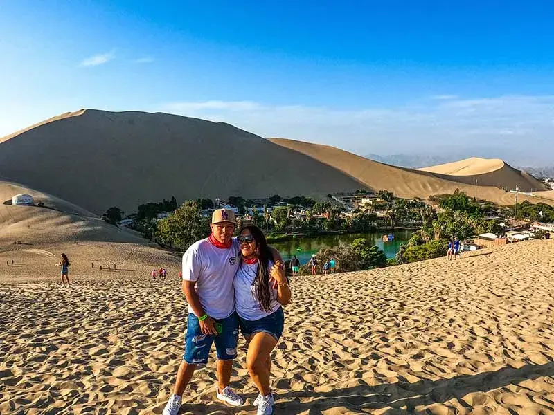 Pareja de turistas en las dunas con vista a la laguna de Huacachina durante el Full Day Paracas Ica Chincha desde Lima