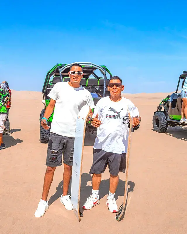Turistas con tablas de sandboarding junto a buggies en Huacachina durante el tour full day