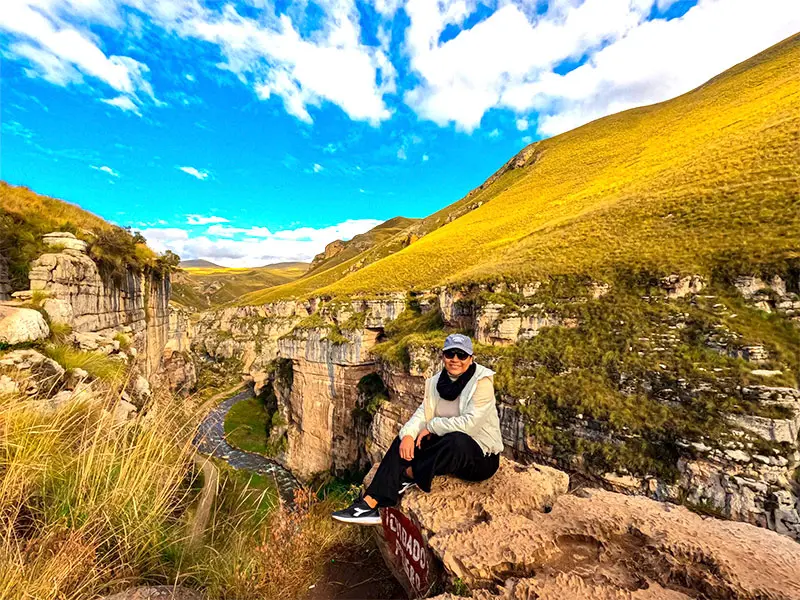 Turista sentada al borde del imponente Cañón de Shutjo durante un tour Full Day en Jauja, Junín.